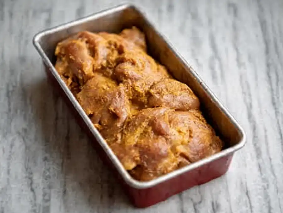 Raw marinated chicken thighs layered in a loaf pan,
